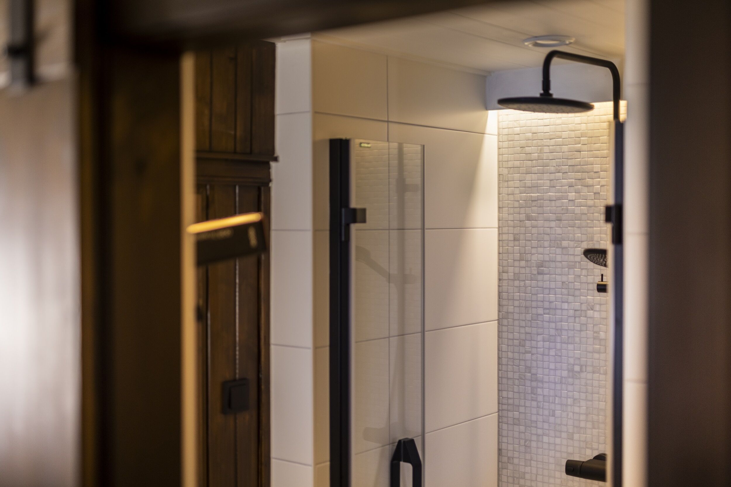 Un baño moderno con cabina de ducha de vidrio, paredes de azulejos blancos y una puerta de madera.