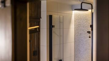 Un baño moderno con cabina de ducha de vidrio, paredes de azulejos blancos y una puerta de madera.
