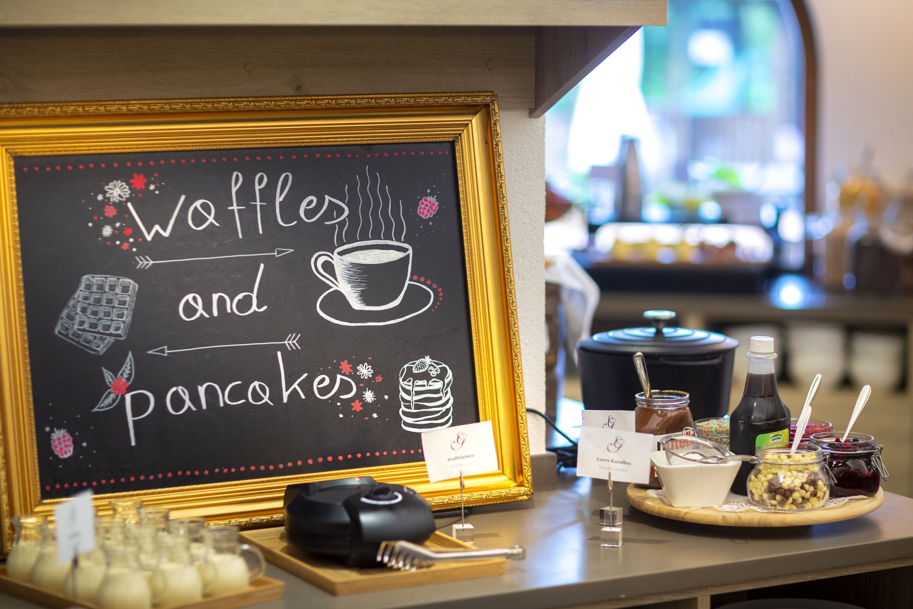 A chalkboard sign with waffles and pancakes, a cash register, and various condiments on a counter.