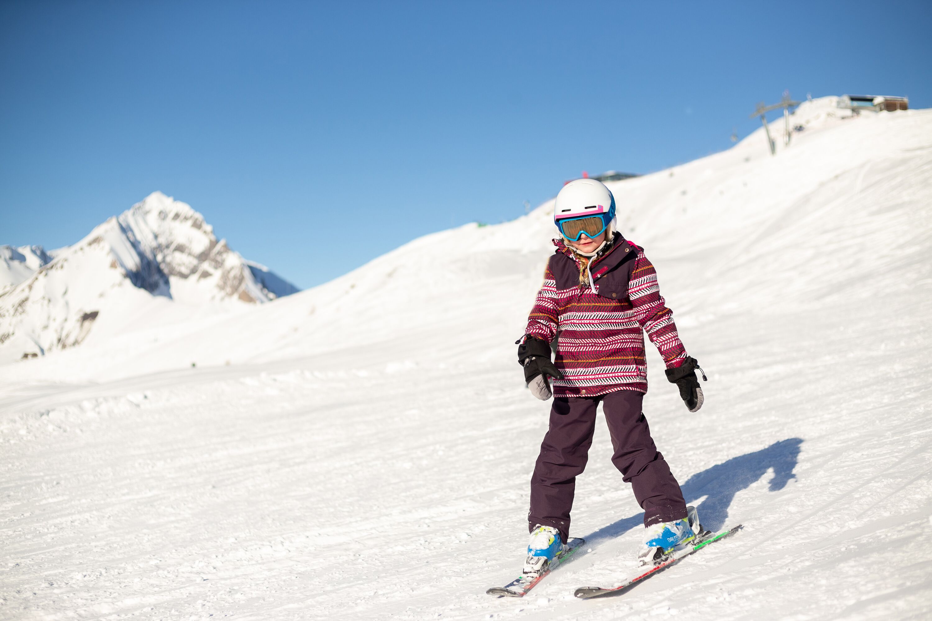 A person skiing on a snowy slope with a clear sky and mountains in the background.
