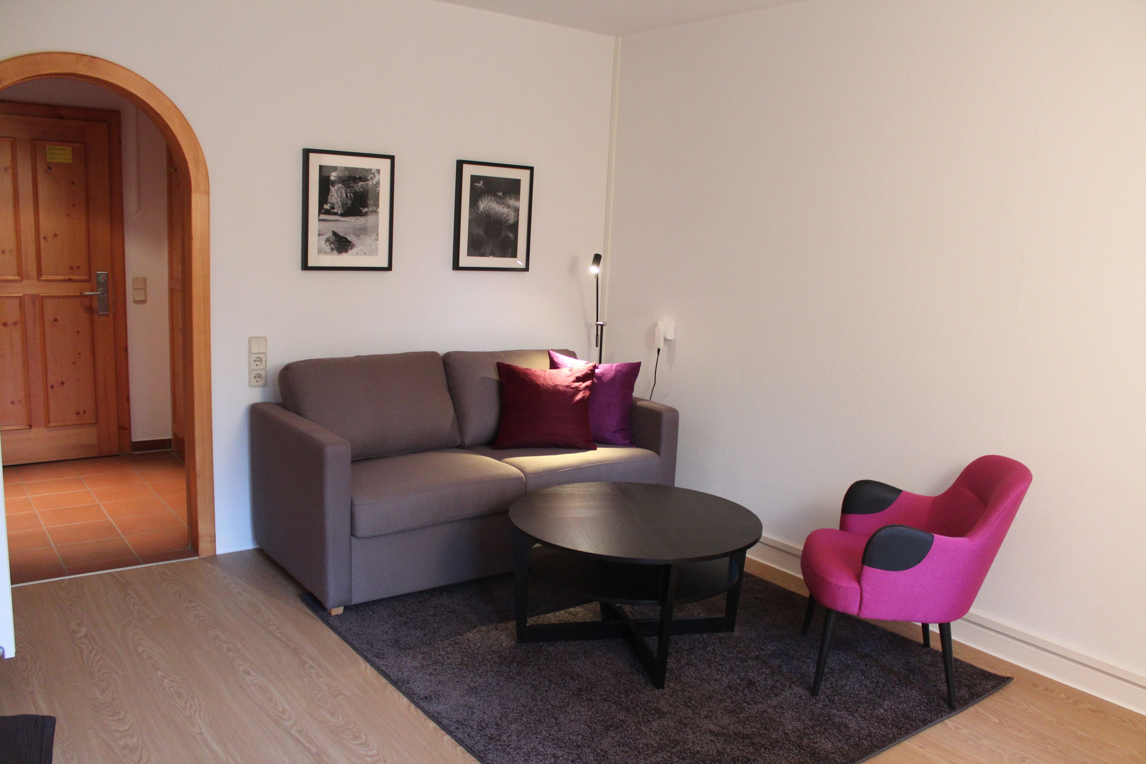 Una sala de estar con un sofá, una mesita de centro y dos sillones. Hay dos cuadros en la pared.