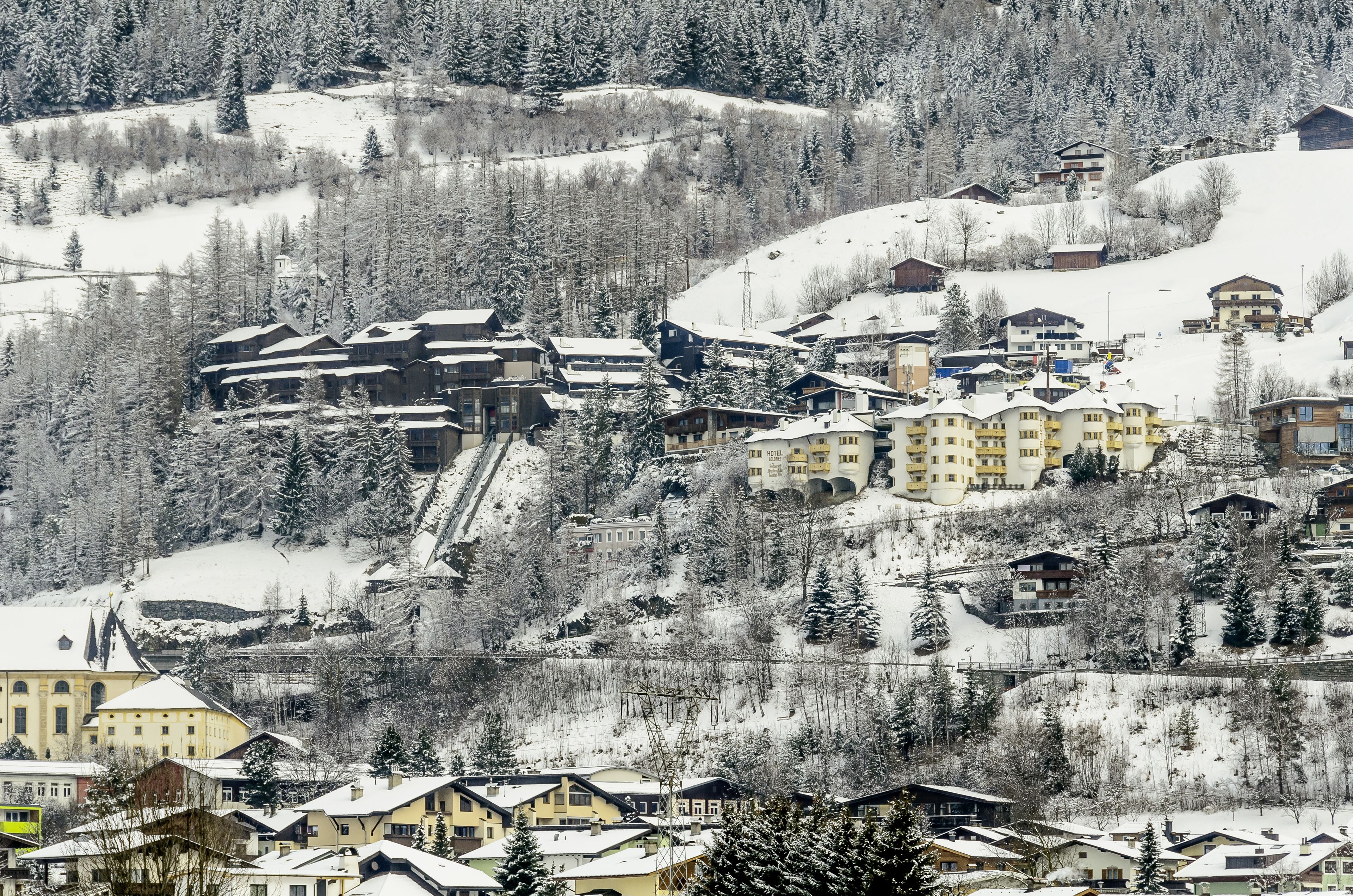 Un pueblo cubierto de nieve en la montaña, con edificios, incluyendo un hotel grande de varios pisos y un telesilla visible.