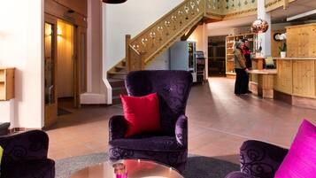 A lobby with a purple armchair, a glass coffee table, and a wooden staircase.