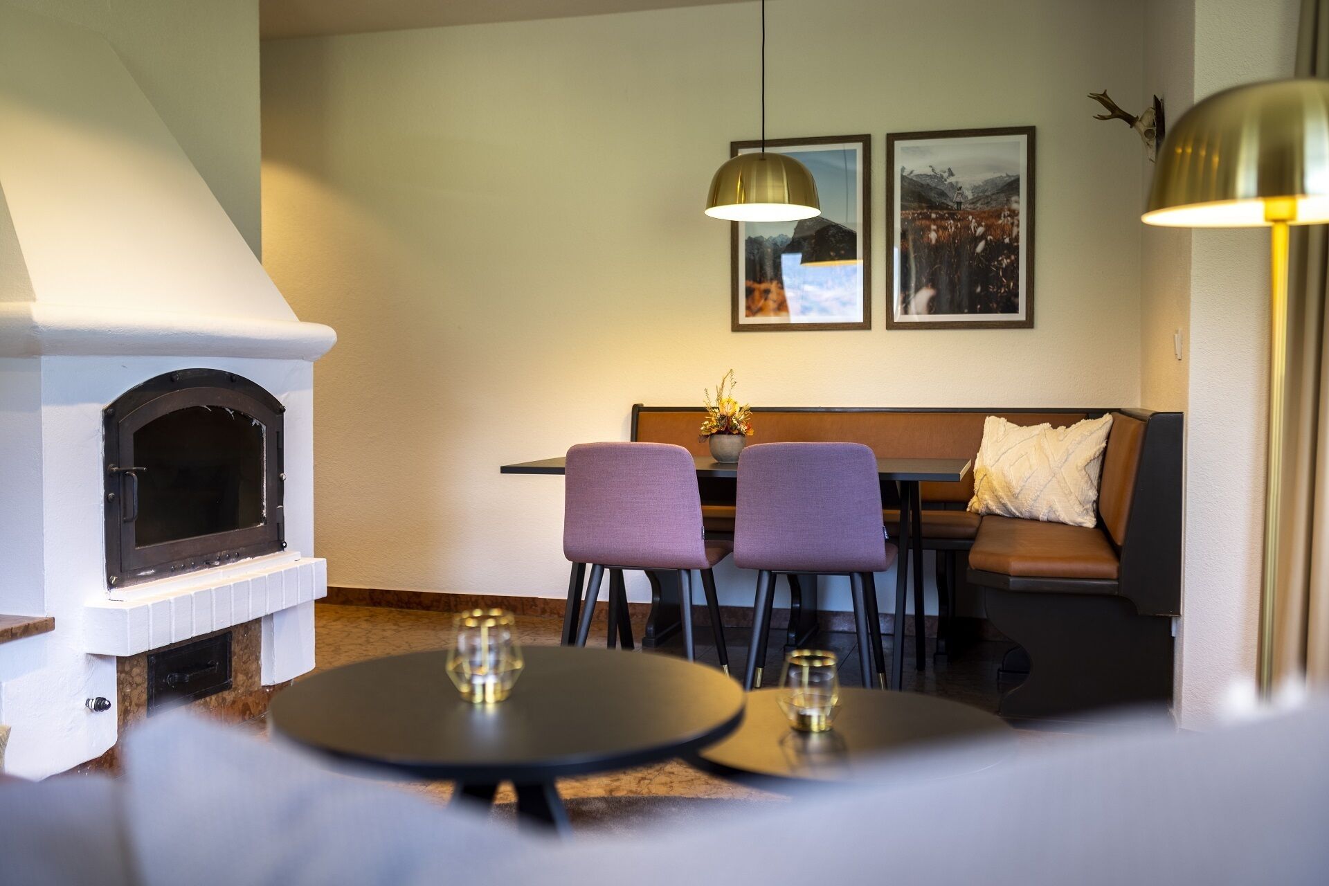 A cozy living room with a fireplace, a sofa, two chairs, a dining table, and two framed pictures on the wall.
