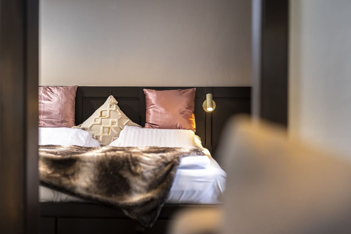 A neatly made bed with a patterned pillow, a textured throw blanket, and a modern light fixture above.