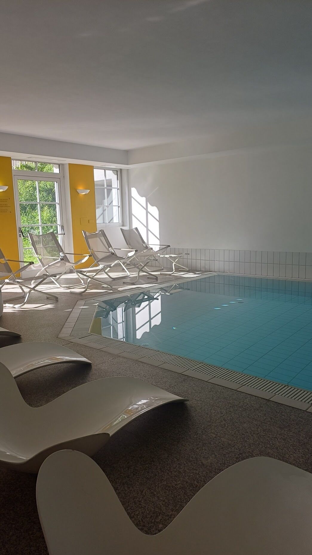 Una piscina interior con sillones de descanso y vistas a zonas verdes.