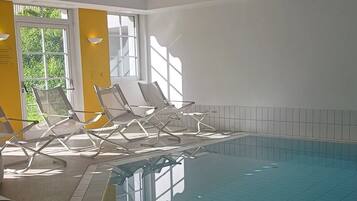 Una piscina interior con sillones de descanso y vistas a zonas verdes.