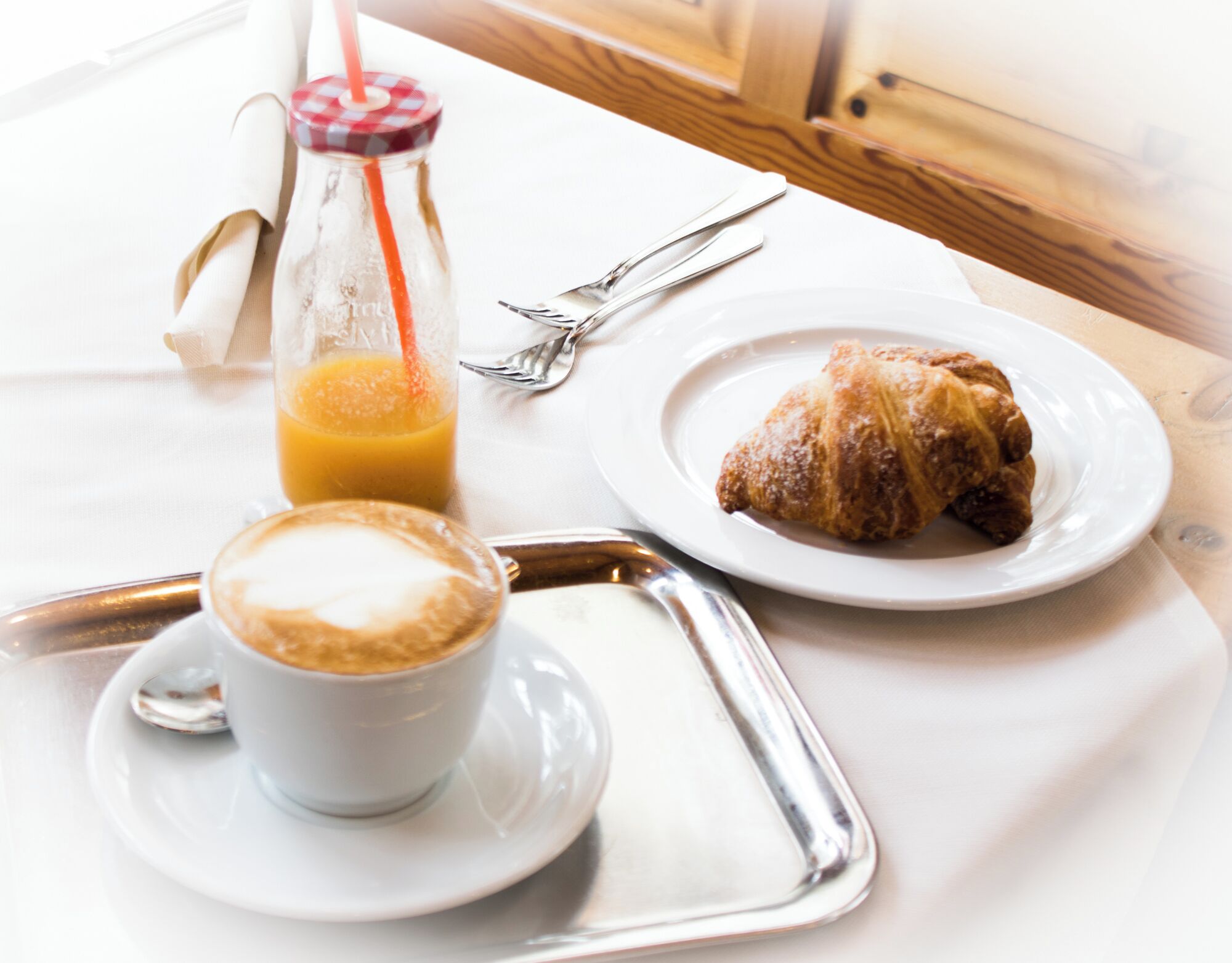 A breakfast tray with a croissant, a cup of coffee, and a glass of orange juice on a white tablecloth.