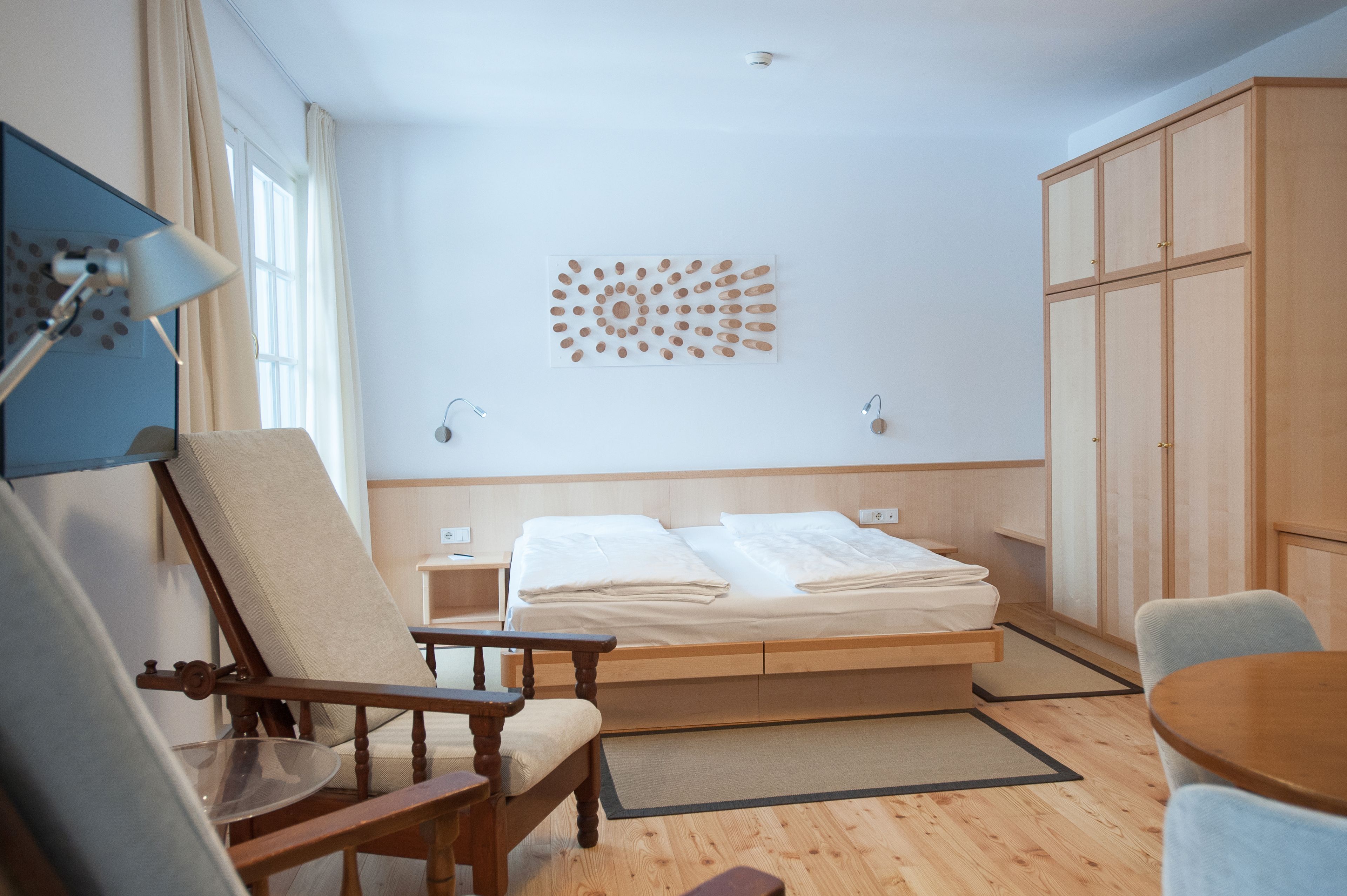 A hotel room with a bed, a chair, a table, and a wall art piece.