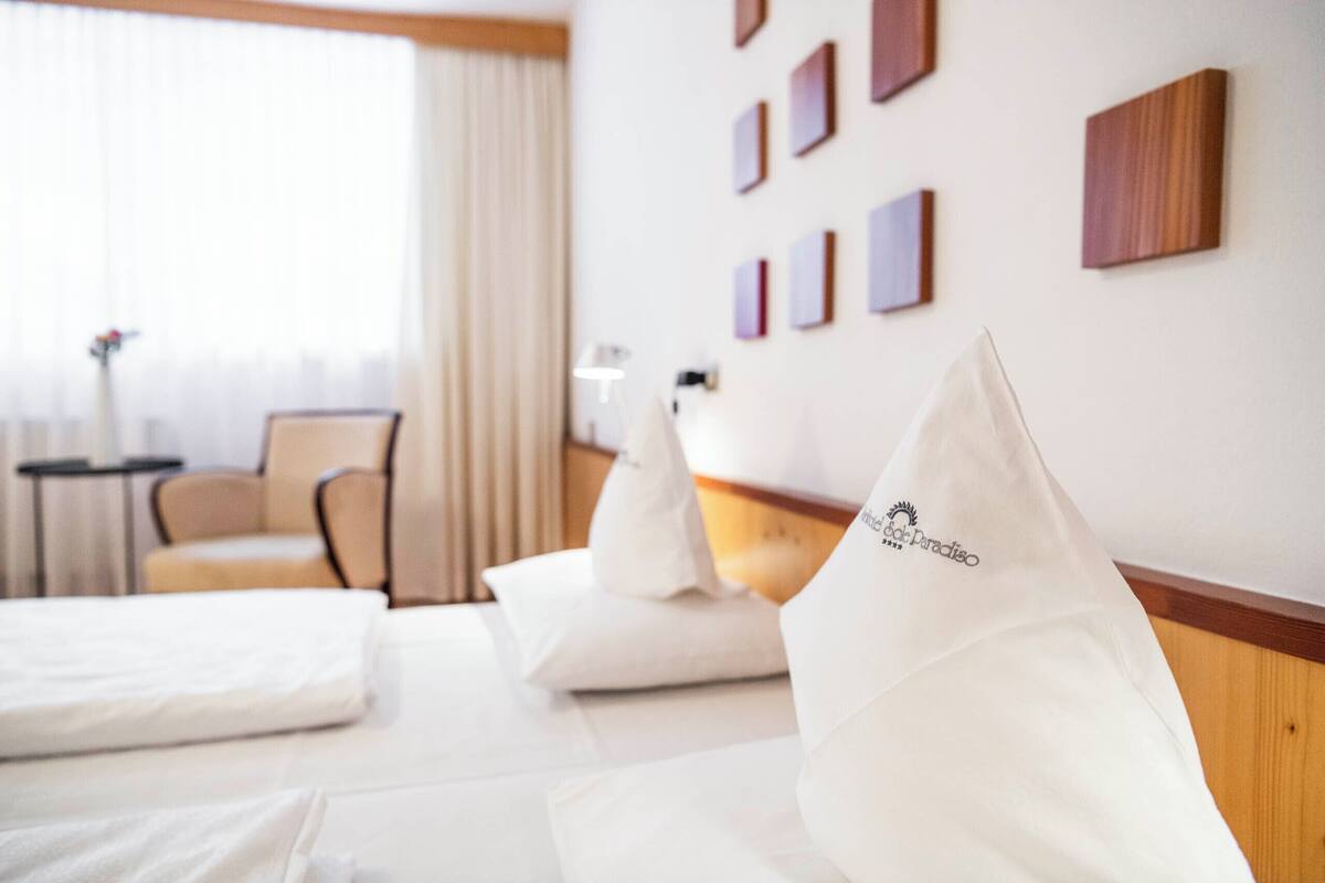 A hotel room with a bed, pillows, a chair, a nightstand, and a wall with framed pictures.