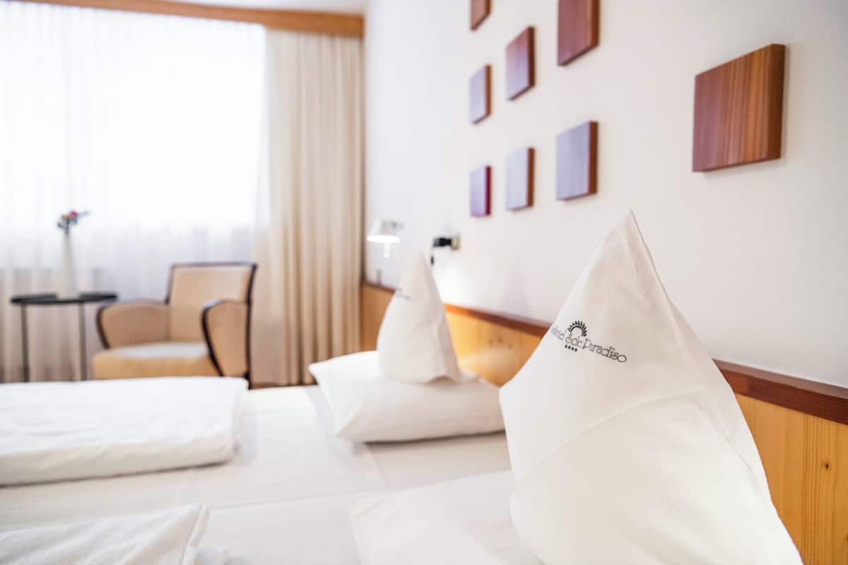 A hotel room with a bed, pillows, a chair, a nightstand, and a wall with framed pictures.
