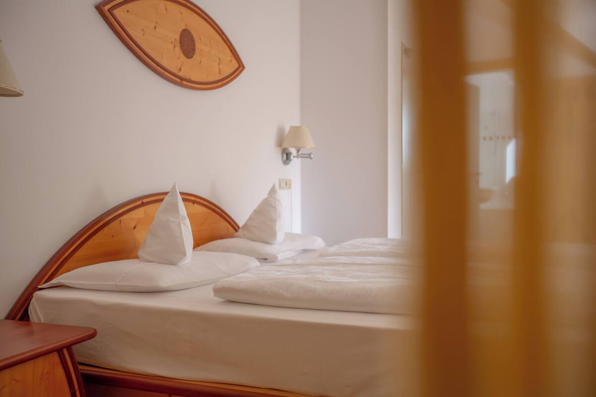 A bed with a wooden headboard, white bedding, and a wall-mounted lamp.