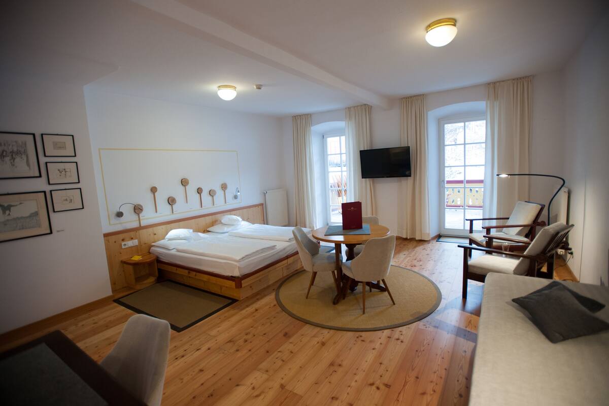 A hotel room with a bed, a desk, two chairs, a TV, and a window.
