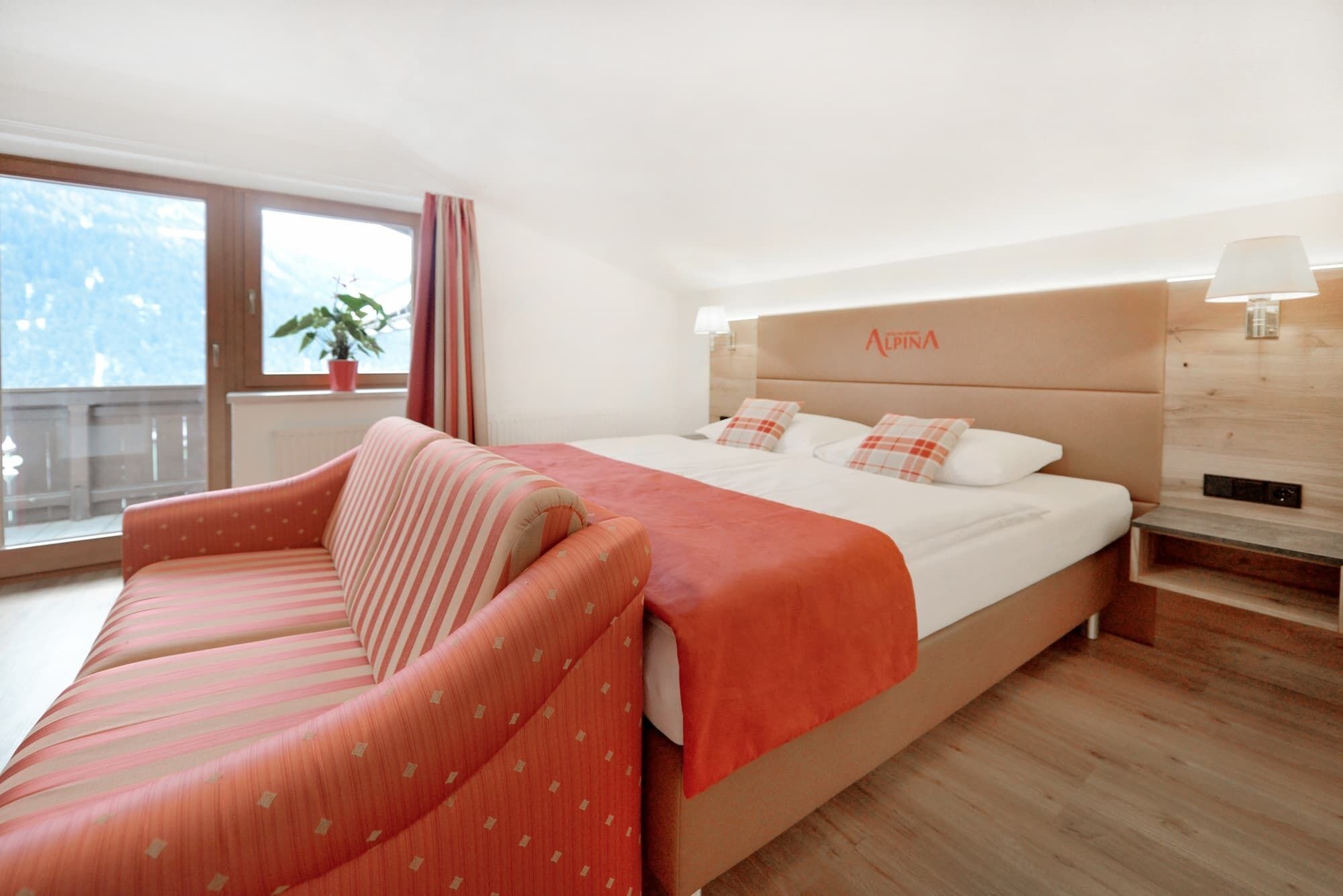 Habitación de hotel con una cama grande, un sofá, una ventana con vistas y un cabecero con el nombre de la marca.