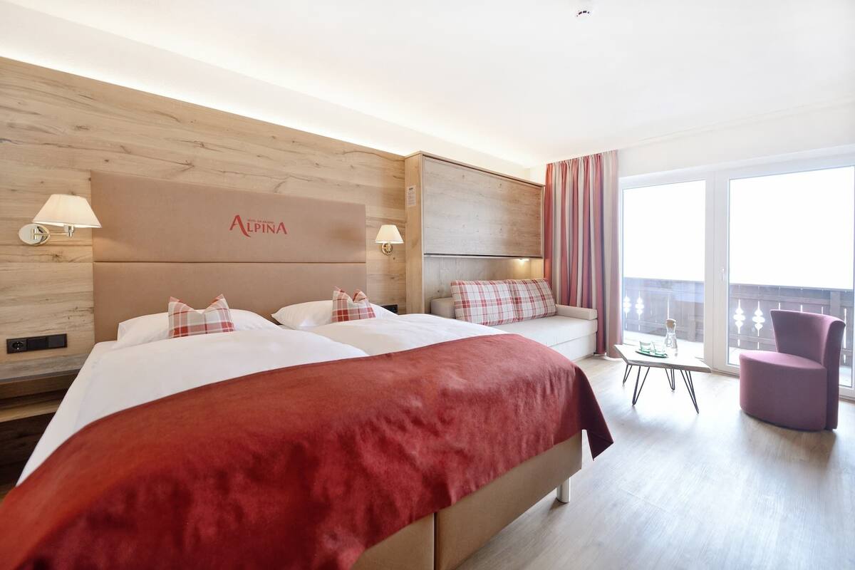 A hotel room with a large bed, a sofa, a small table, and a balcony with a chair.