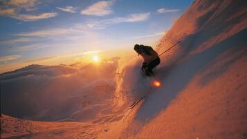 Ein Skifahrer bewegt sich auf einem steilen, mit Schnee bedeckten Hang fort, am klaren Himmel geht die Sonne unter.