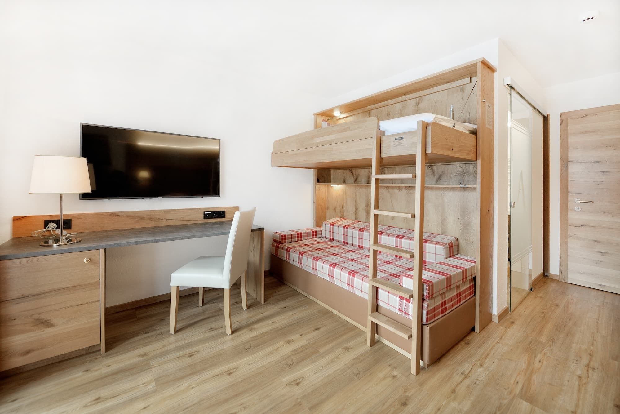 A bunk bed with a desk and chair, a flat-screen TV, and a wooden wardrobe.