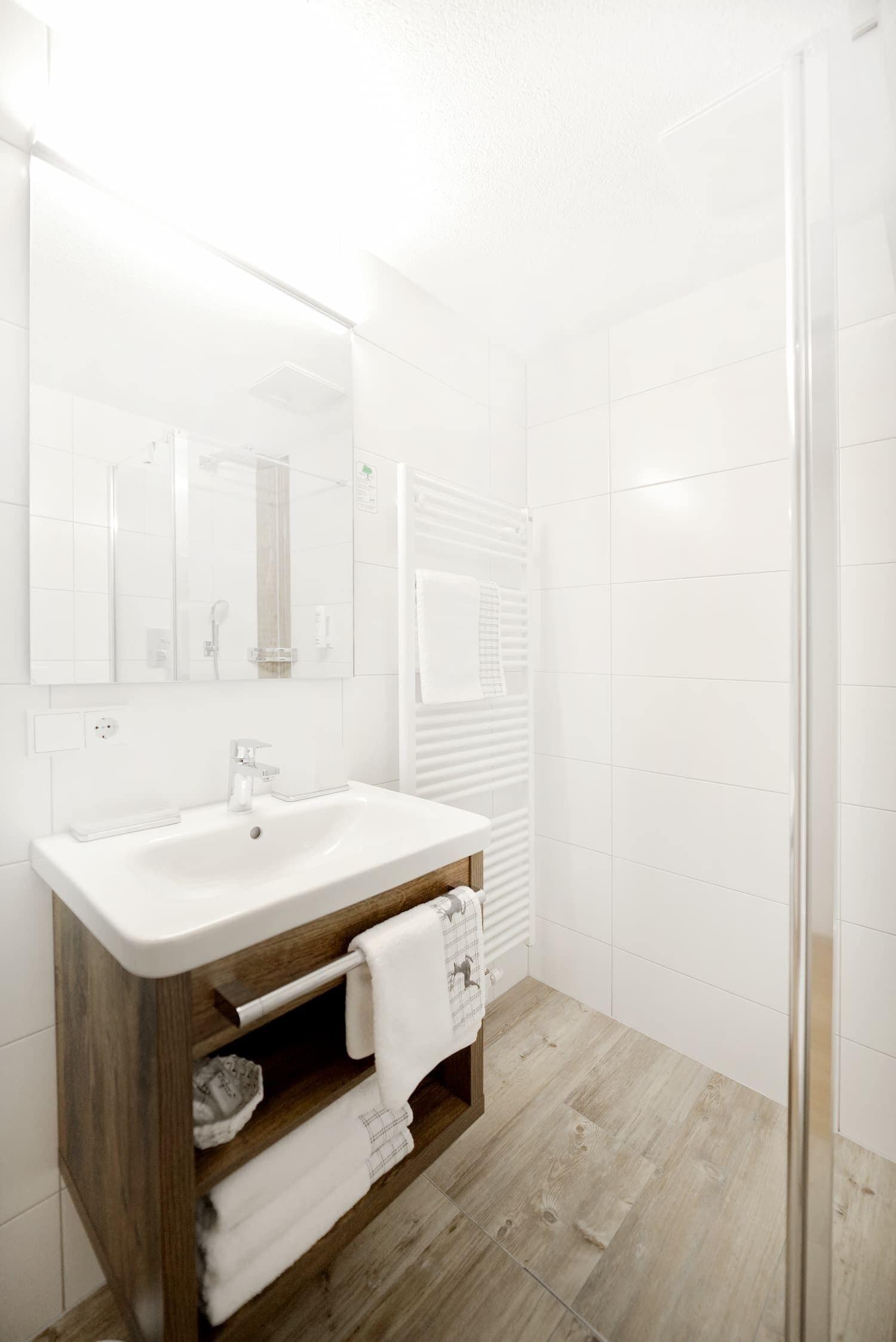 A modern bathroom with a white sink, wooden vanity, and a glass shower enclosure.