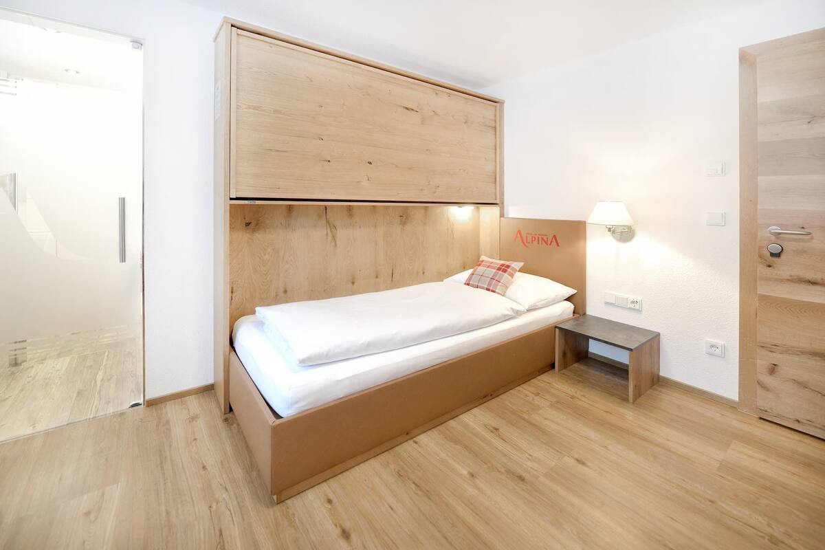 A single-bed room with a wooden headboard, a bedside table with a lamp, and a wardrobe with a mirror.