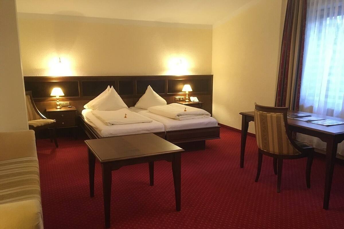 A hotel room with two beds, a small table, a chair, and a desk.