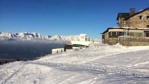 Un paisaje montañoso cubierto de nieve con un edificio de piedra, un telesilla y un cielo azul despejado.