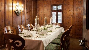 Comedor con una larga mesa dispuesta para una comida, paredes de paneles de madera y un ventanal con vidrieras.