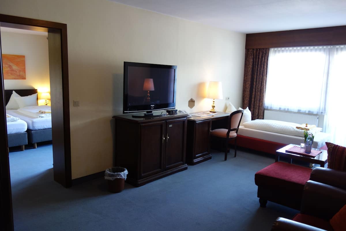A hotel room with a television, two beds, a desk, a chair, and a window with curtains.