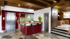 Una cocina moderna con una isla roja, un ascensor de acero inoxidable y un piso de baldosas de piedra.