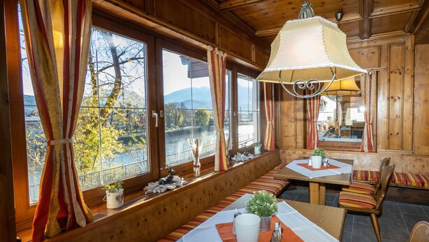 Un interior de madera con ventanas amplias, una zona de comedor con mesa y sillas, y un banco junto a la ventana.
