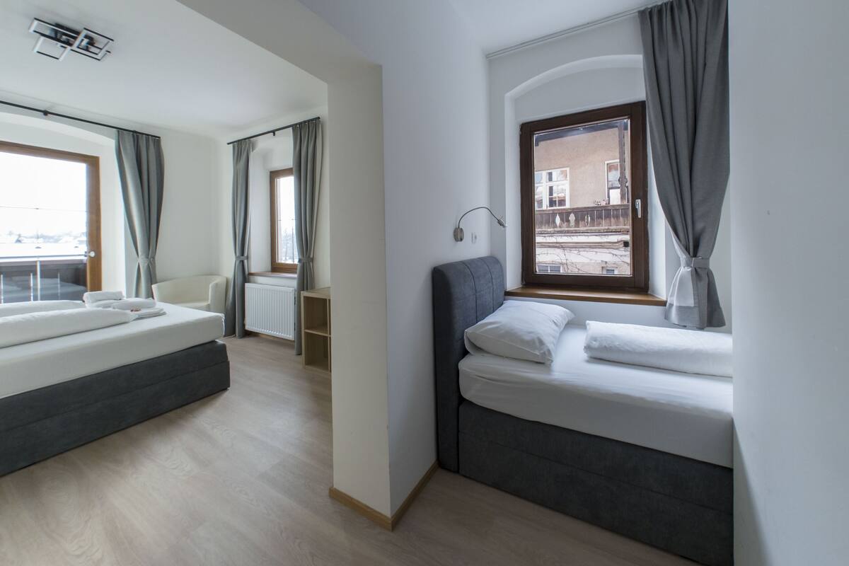 A modern hotel room with a large bed, a smaller bed, and a window with curtains.