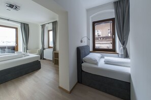 A modern hotel room with a large bed, a smaller bed, and a window with curtains. - Hotel Heimgartl (Innsbruck)