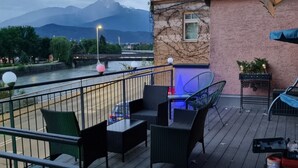 Una terraza con mobiliario exterior, vista a un río y montañas al fondo.