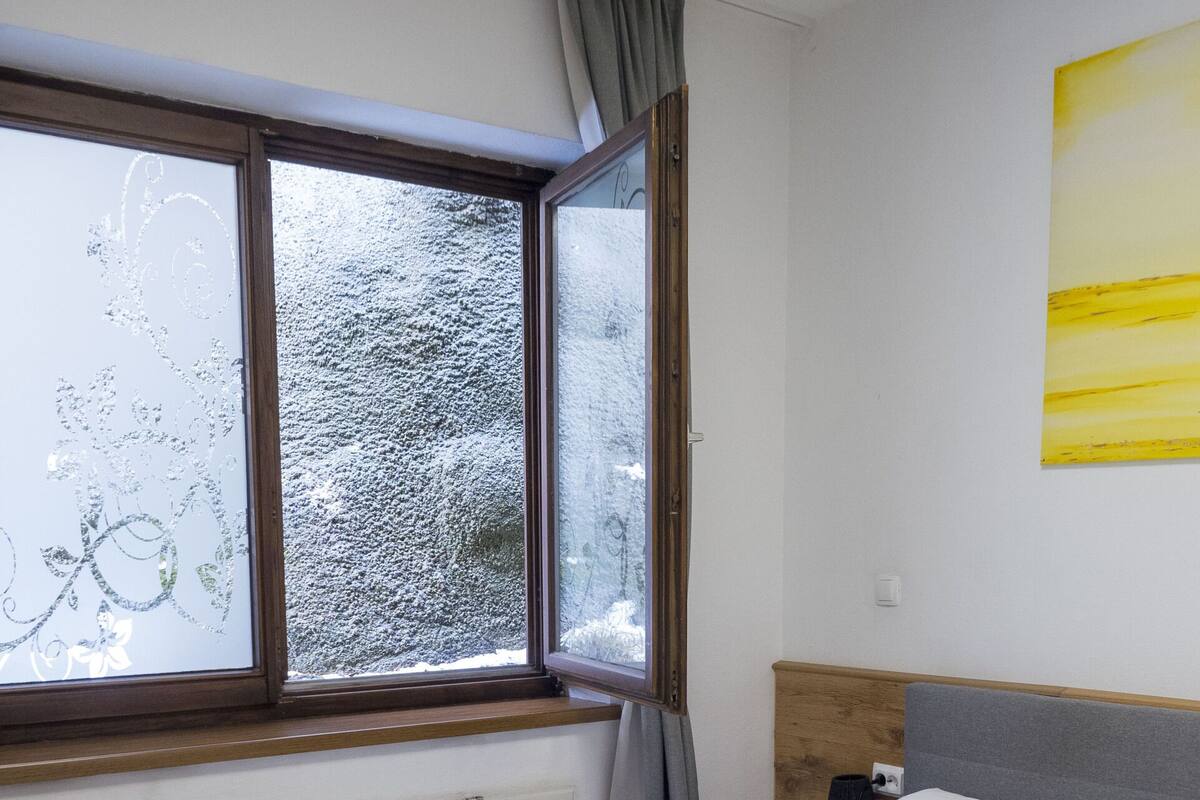 A neatly made bed with white linens and towels, a window with frosted glass, and a wooden headboard.