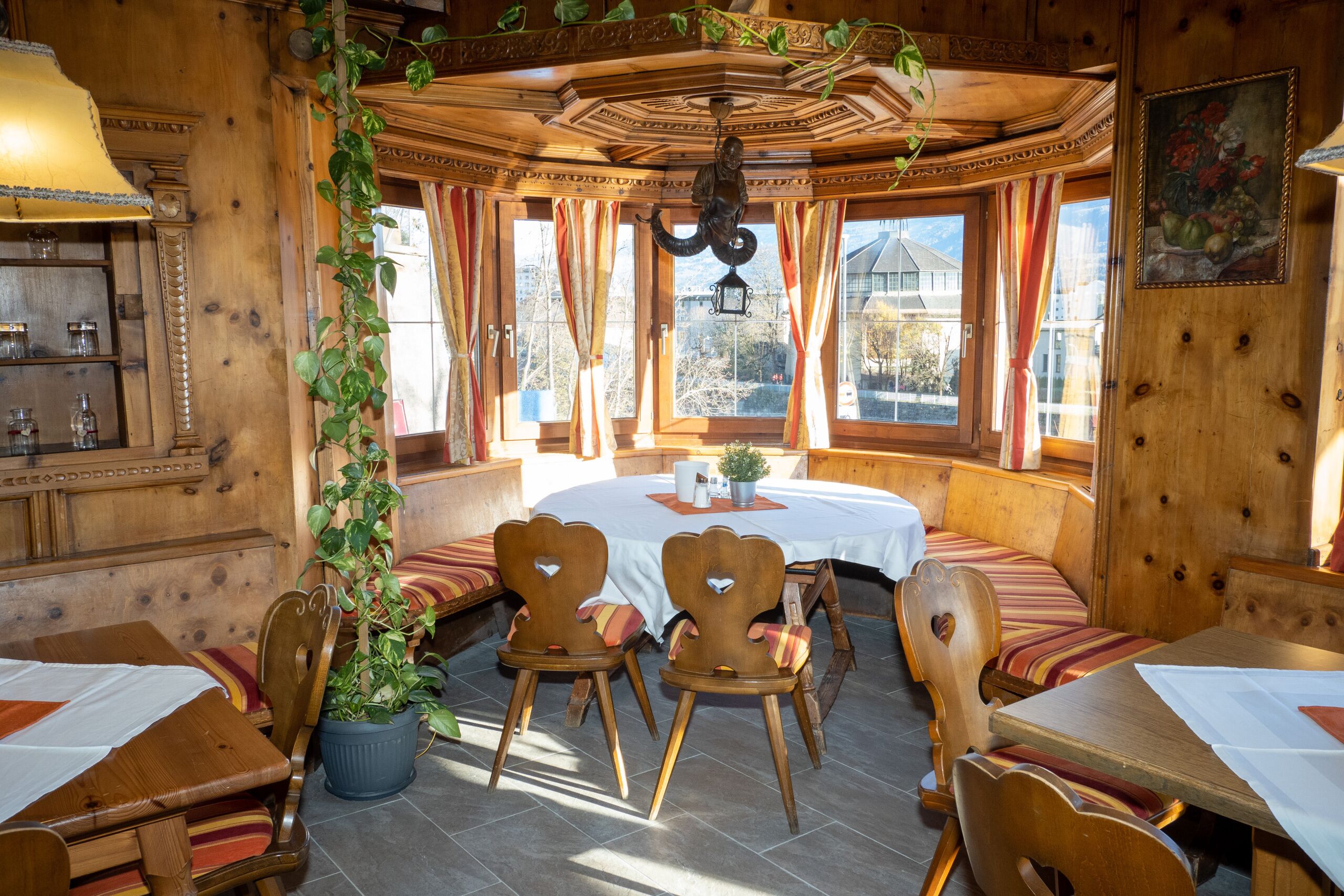 Un comedor acogedor con muebles de madera, una planta en maceta y vistas al exterior a través de grandes ventanales.