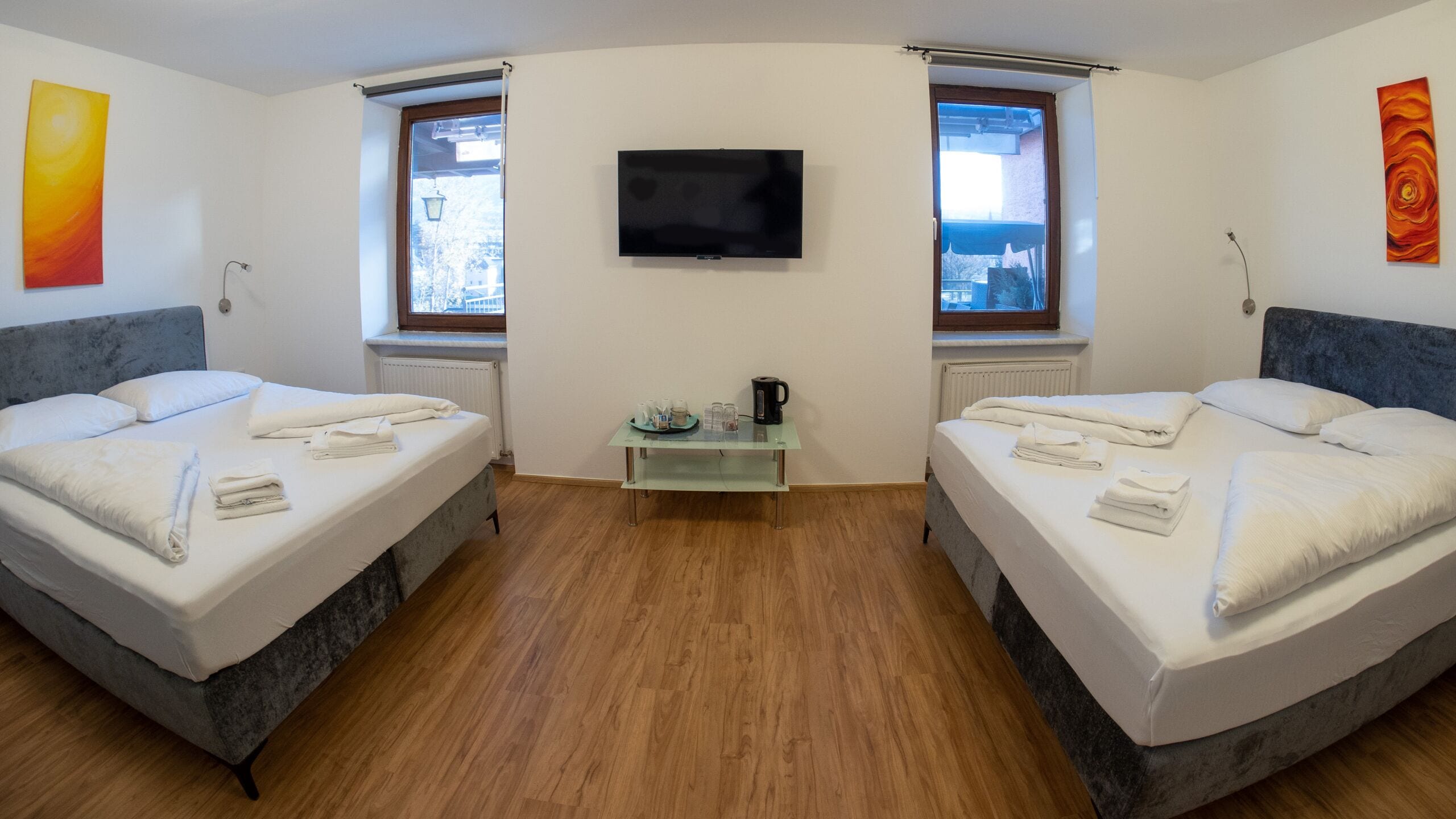 A hotel room with two beds, a TV, and a small table with a kettle and cups.