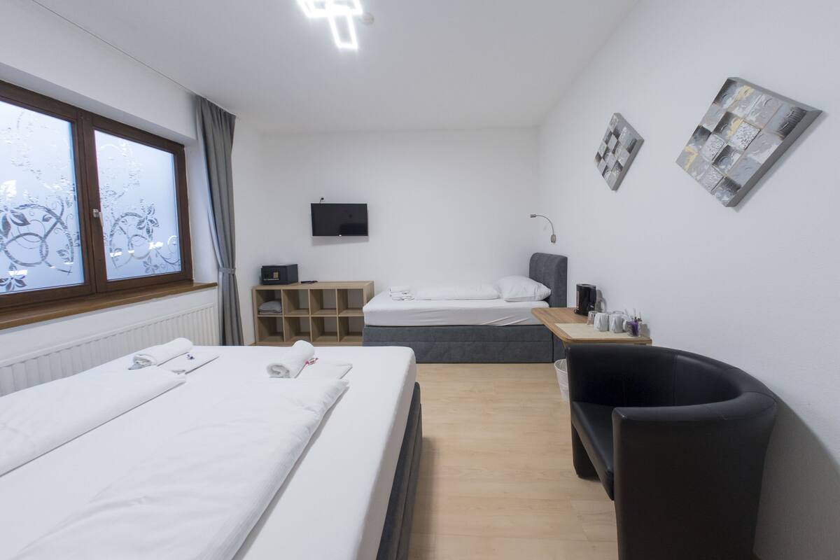 A hotel room with two beds, a desk, a chair, a TV, and artwork on the walls.