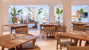 Un restaurant moderne avec des tables et des chaises en bois, de grandes fenêtres et des plantes d’intérieur.