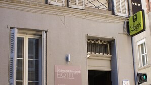 La façade d’un hôtel, avec une enseigne indiquant « Hôtel Edmond Rostand » et une autre indiquant « Logis ».