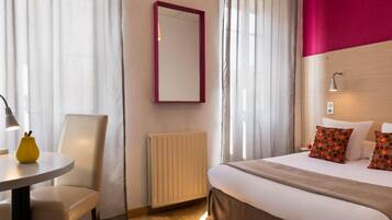 Quarto de hotel com cama, cadeira, mesa com abajur, espelho e radiador.
