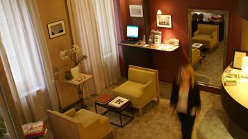 A hotel room with a desk, two armchairs, a small table with a vase of flowers, and a large mirror on the wall.