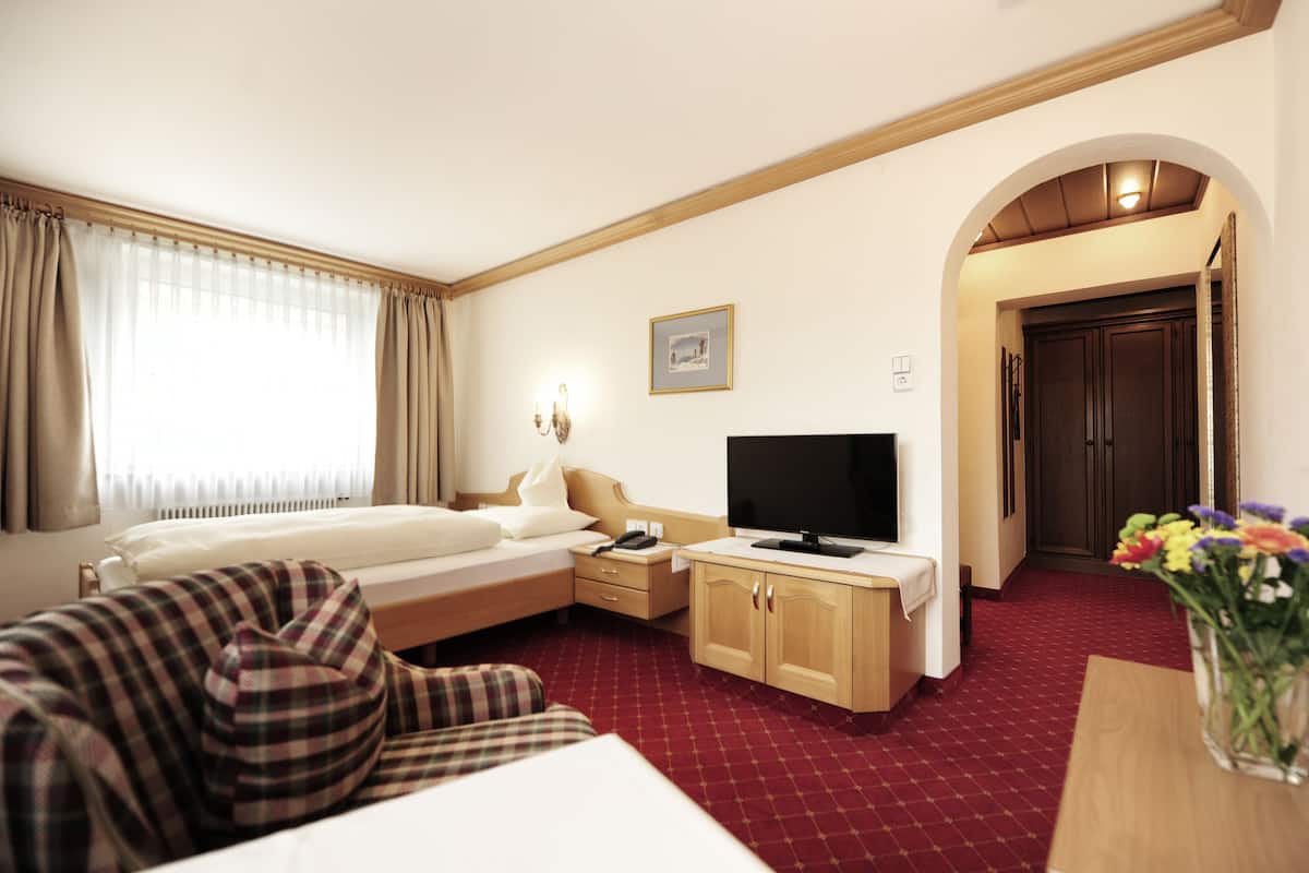A hotel room with a bed, a desk, a television, and a red carpeted floor.