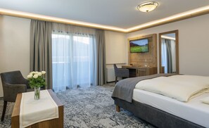 Habitación de hotel con cama, escritorio, silla, televisor y ventana con cortinas.