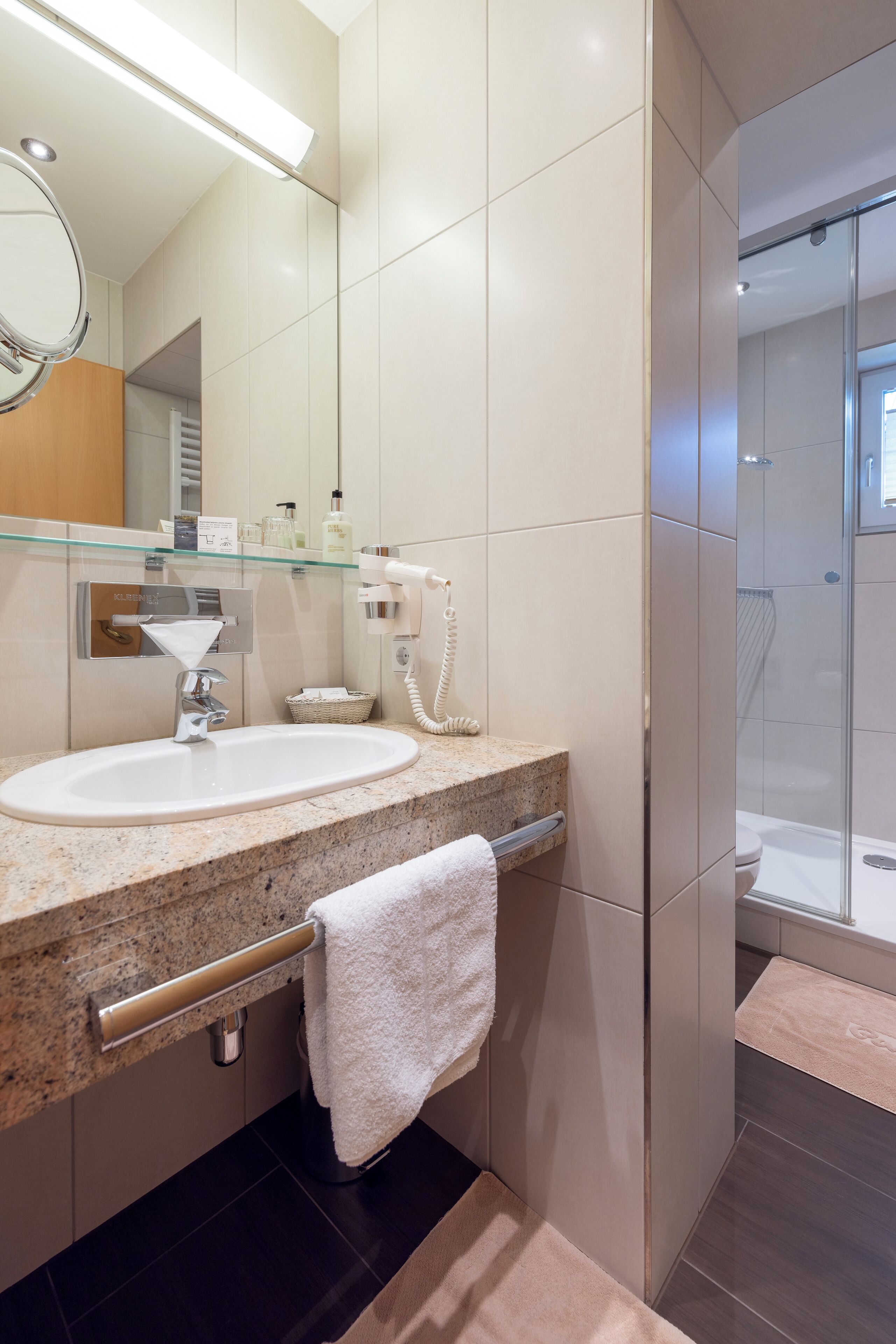 Ein modernes Badezimmer mit einer Granit-Arbeitsplatte, einem weißen Waschbecken, einer Duschkabine aus Glas und einem Handtuchhalter.
