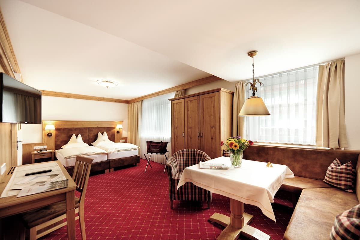 A hotel room with a bed, a desk, a chair, a table with a vase of flowers, and a sofa.
