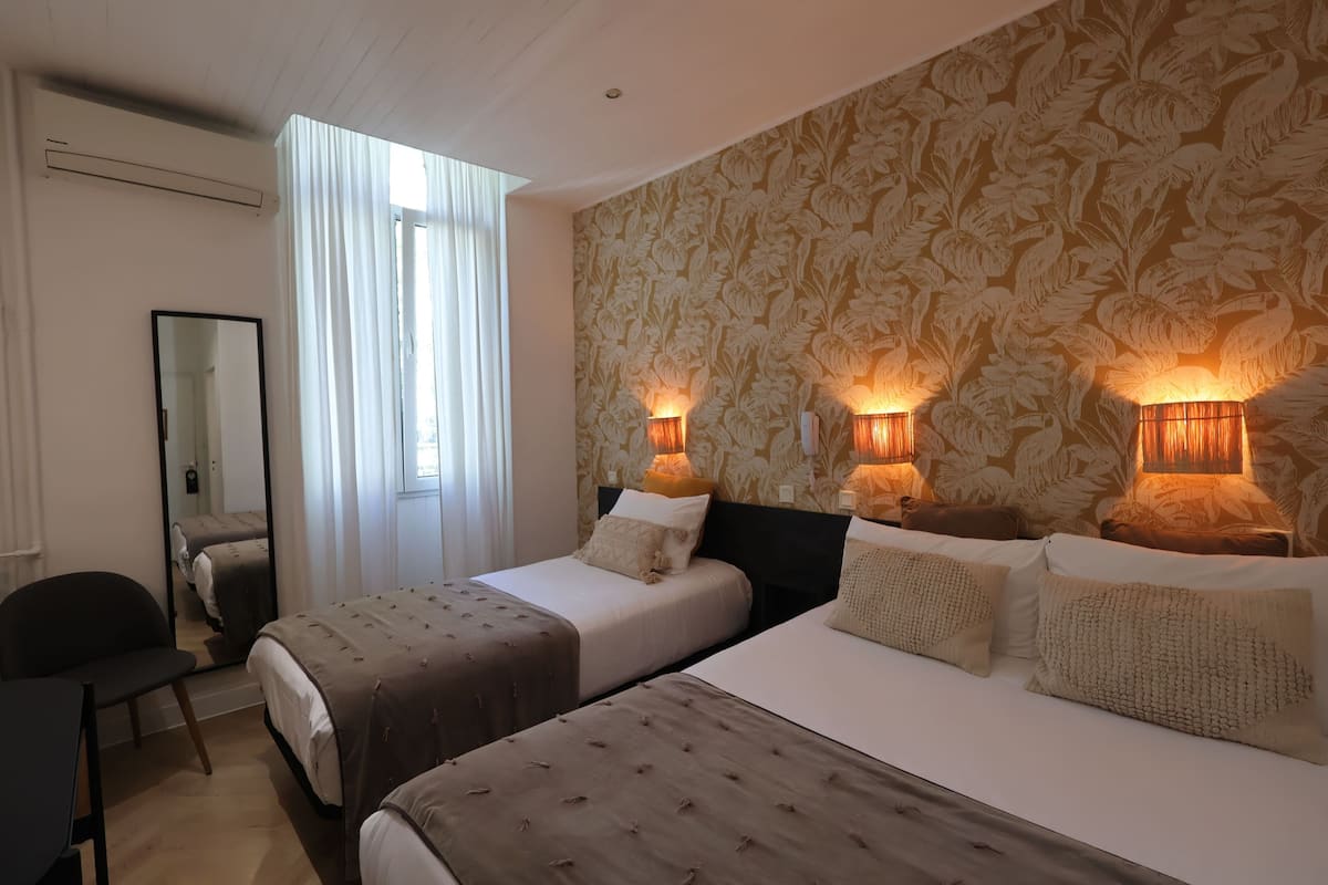 A hotel room with two beds, a mirror, a chair, and a window with curtains.