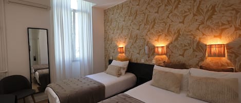 A hotel room with two beds, a mirror, a chair, and a window with curtains.