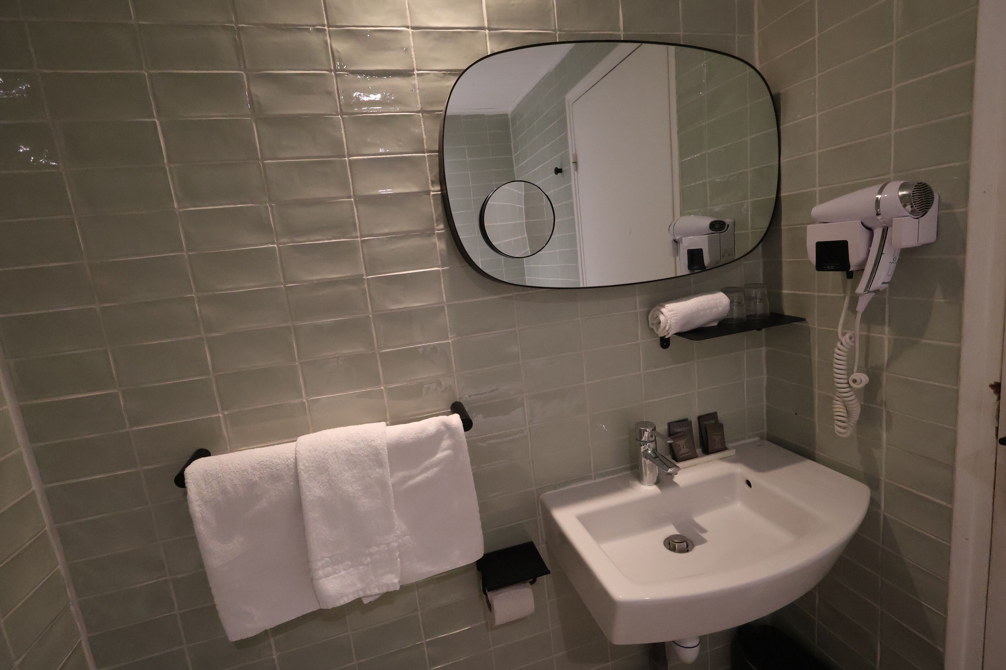 Casa de banho com lavatório, espelho, porta-toalhas e secador de cabelo.