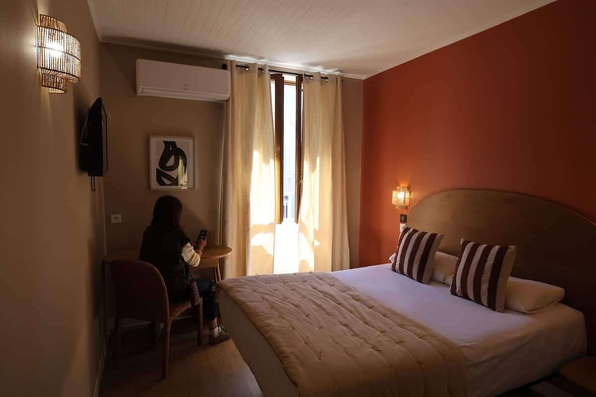 A hotel room with a bed, a desk, a chair, a lamp, and a window with curtains.