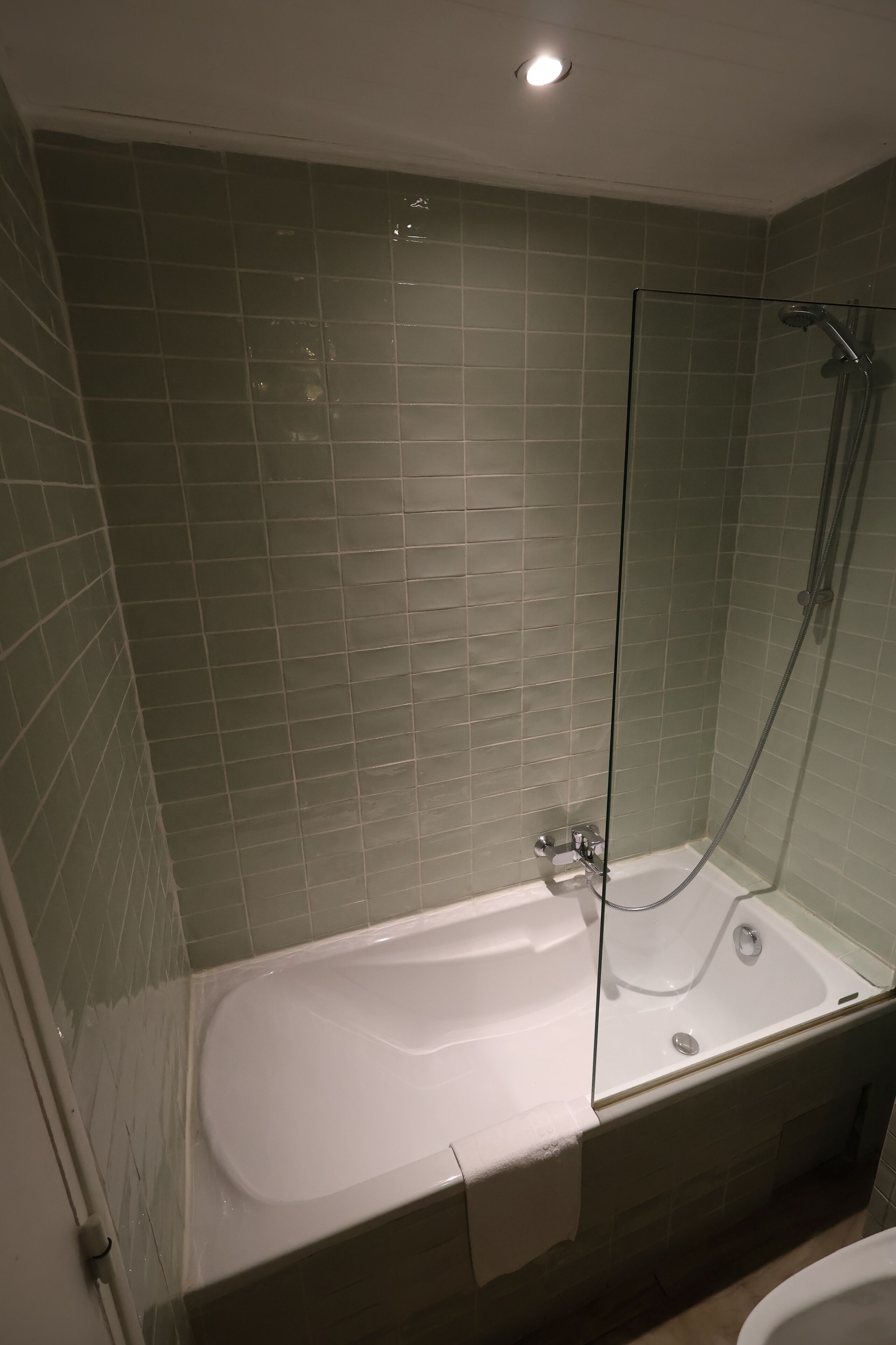 Une salle de bain avec une douche à parois de verre, une baignoire blanche et des murs recouverts de carreaux verts.