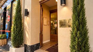 Entrada de hotel con puertas dobles, unos pocos escalones y dos árboles de hoja perenne en macetas.